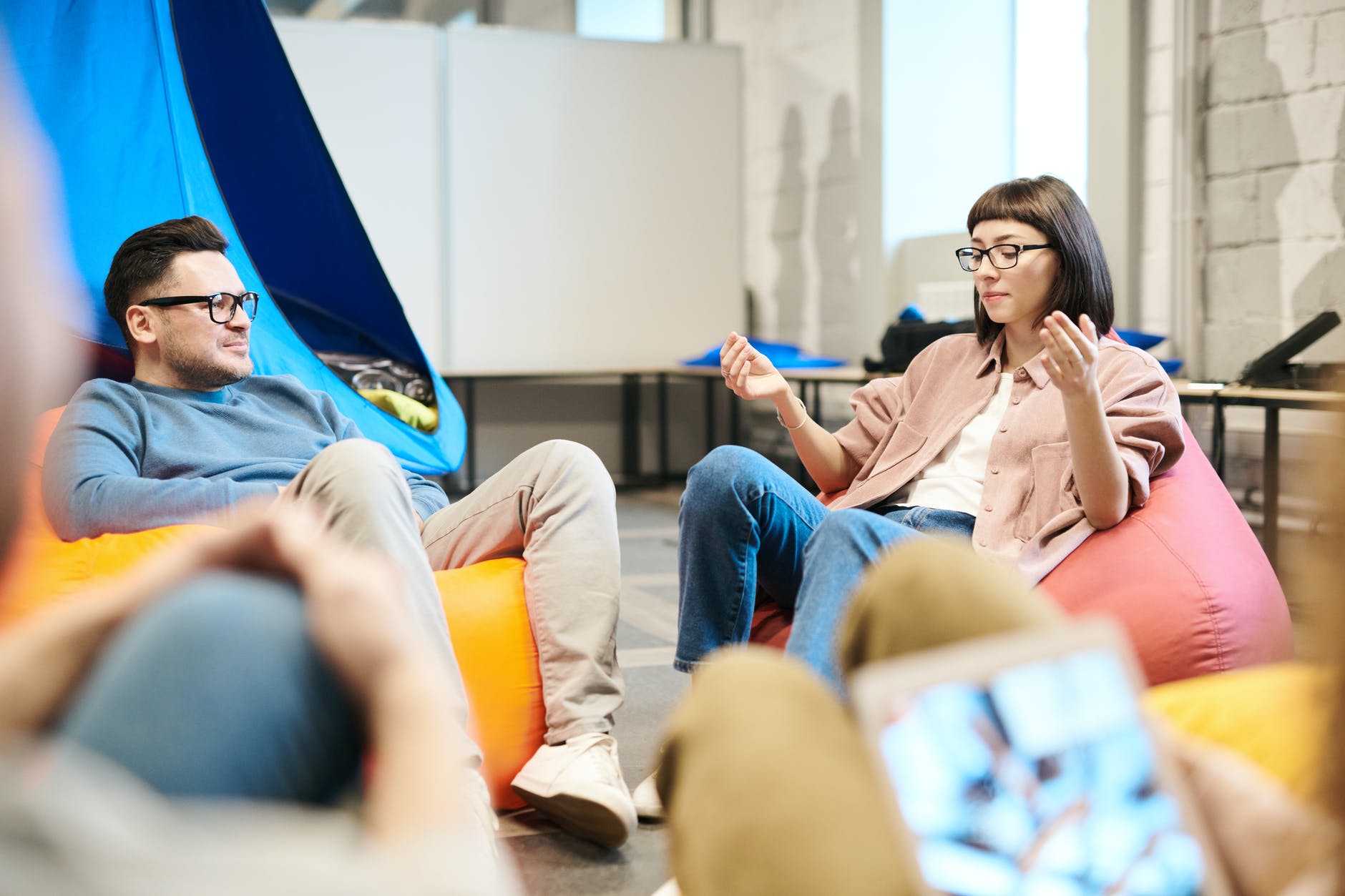 man in blue sweater sitting on beanbag chair beside woman wearing eyeglasses