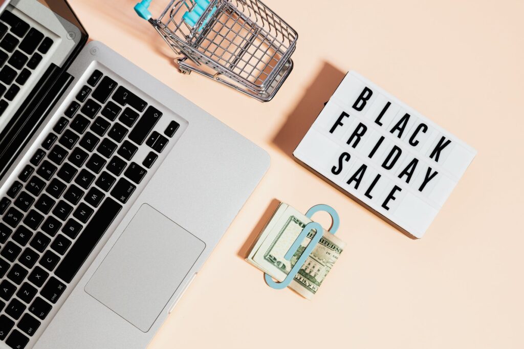 top view of silver macbook beside a shopping cart and black friday sale signage